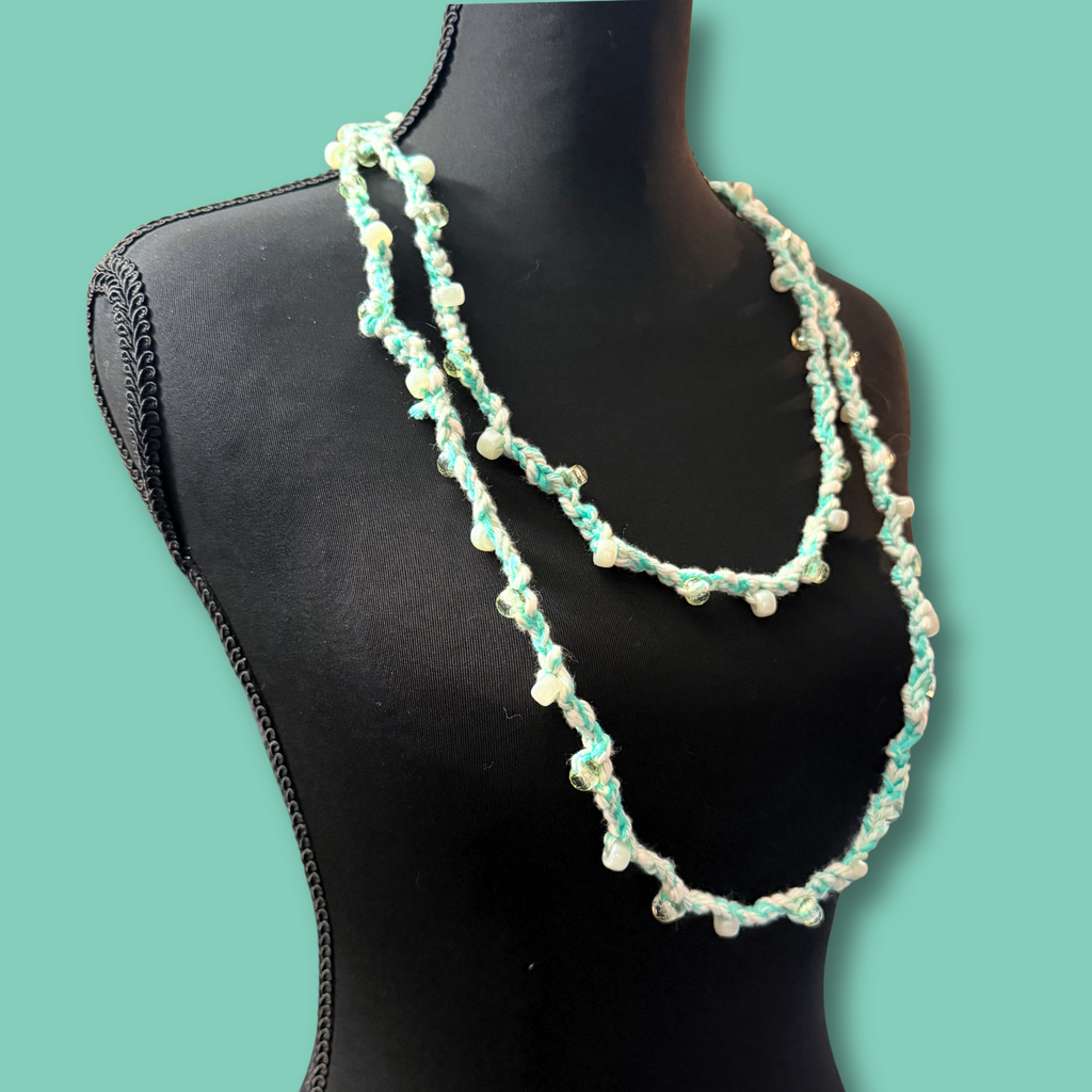 A double-strand beaded necklace with mint green and white beads draped on a black mannequin torso against a solid teal background.
